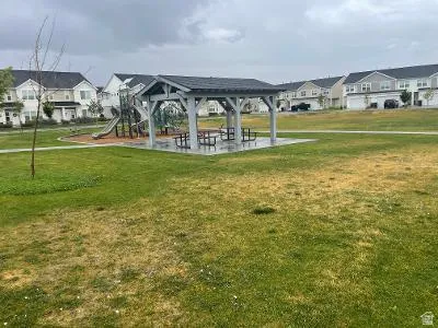 Community green space featuring a covered picnic area with multiple tables, a dedicated children's play structure, and paved pathways