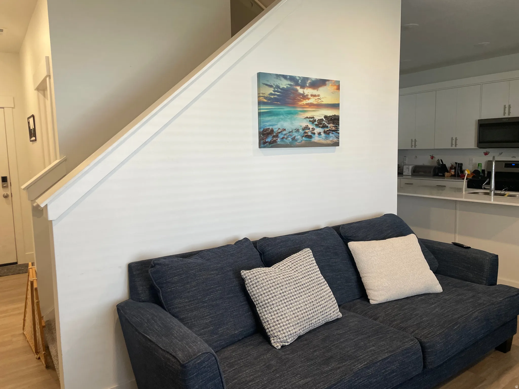 White walls with a partial staircase, L-shaped kitchen, and light wood-finish flooring