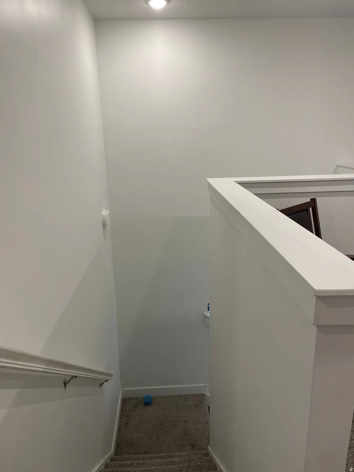 Recessed ceiling lighting illuminates the carpeted stairway with a painted wood handrail and half-wall