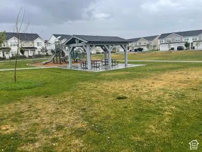 Community green space featuring a covered picnic area with multiple tables, a dedicated children's play structure, and paved pathways