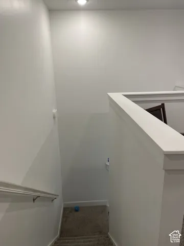 Recessed ceiling lighting illuminates the carpeted stairway with a painted wood handrail and half-wall