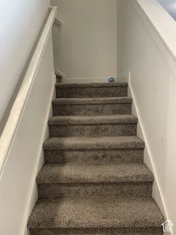 Carpeted staircase featuring neutral toned treads and a clean white painted wall with coordinating handrail for secure passage between levels