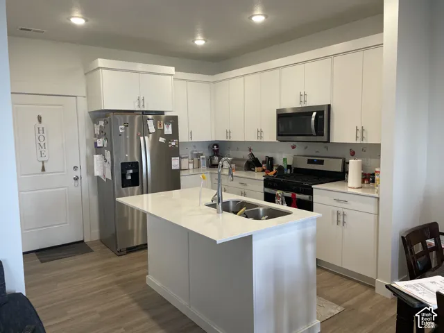 Kitchen featuring a center island with sink, stainless steel appliances, recessed lighting, white cabinetry, and wood-finish flooring