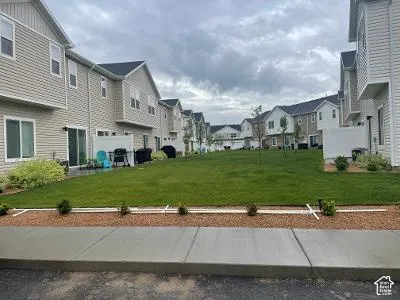 Neutral-toned siding, dark shingle roofing, sliding patio door, concrete patio, and a manicured lawn