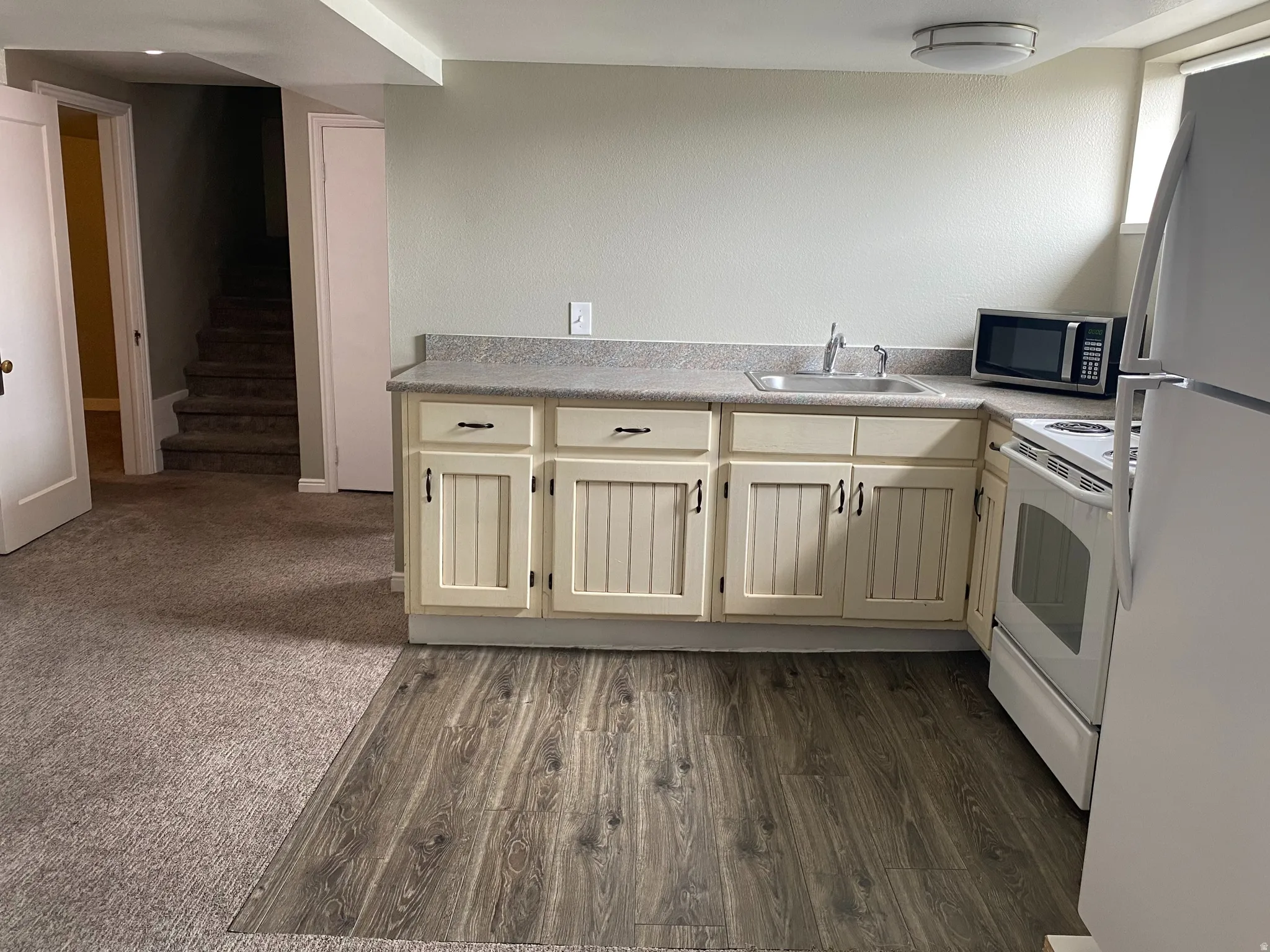 Compact kitchen featuring cream-colored cabinetry, a neutral countertop, stainless steel sink, and wood-finish flooring