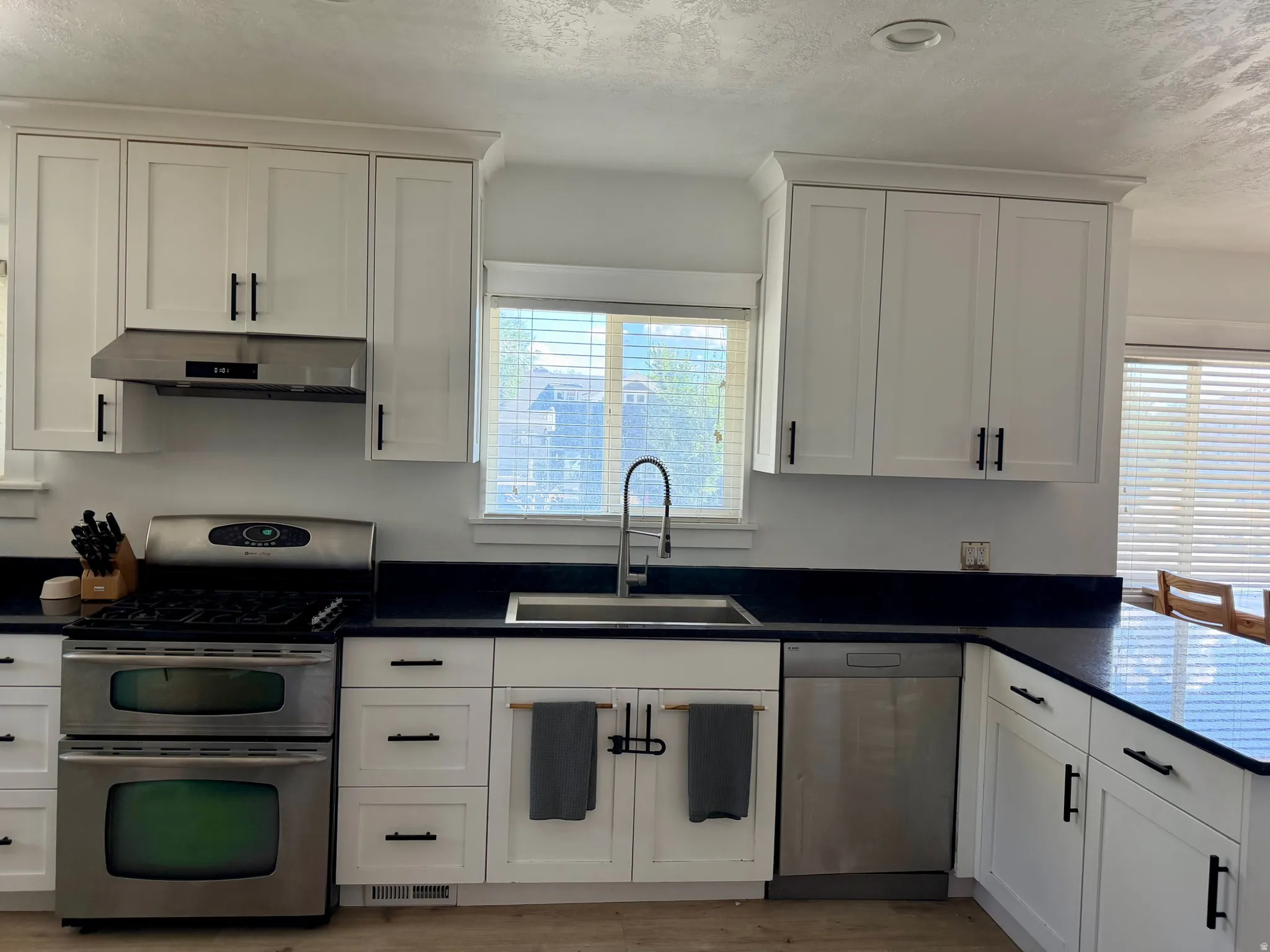 White cabinetry with matte black hardware, stainless steel appliances, dark countertops, and a stainless steel sink with a gooseneck faucet