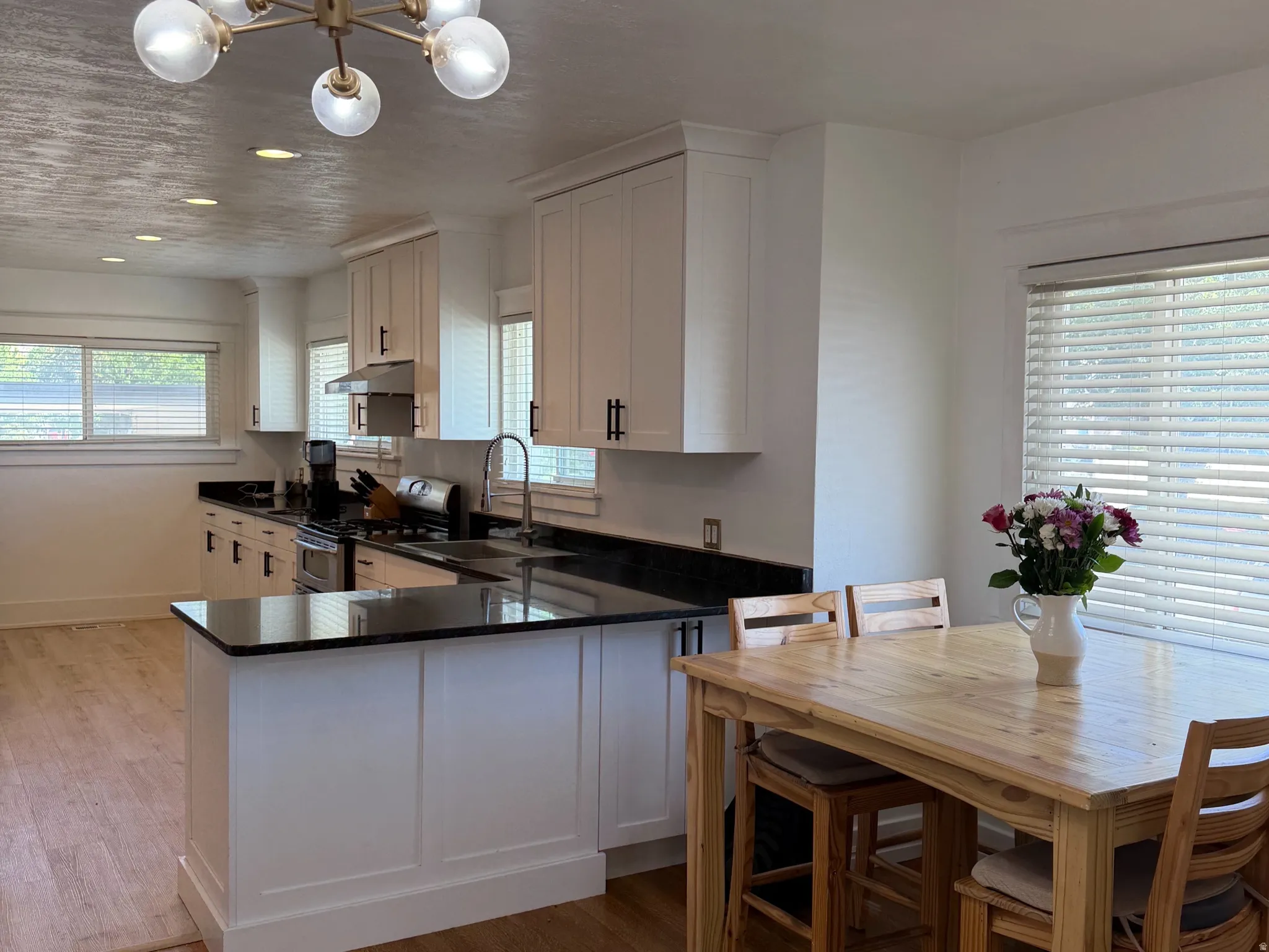 Kitchen featuring wood-finish flooring, white cabinetry with dark hardware, black countertops, and a modern ceiling light fixture