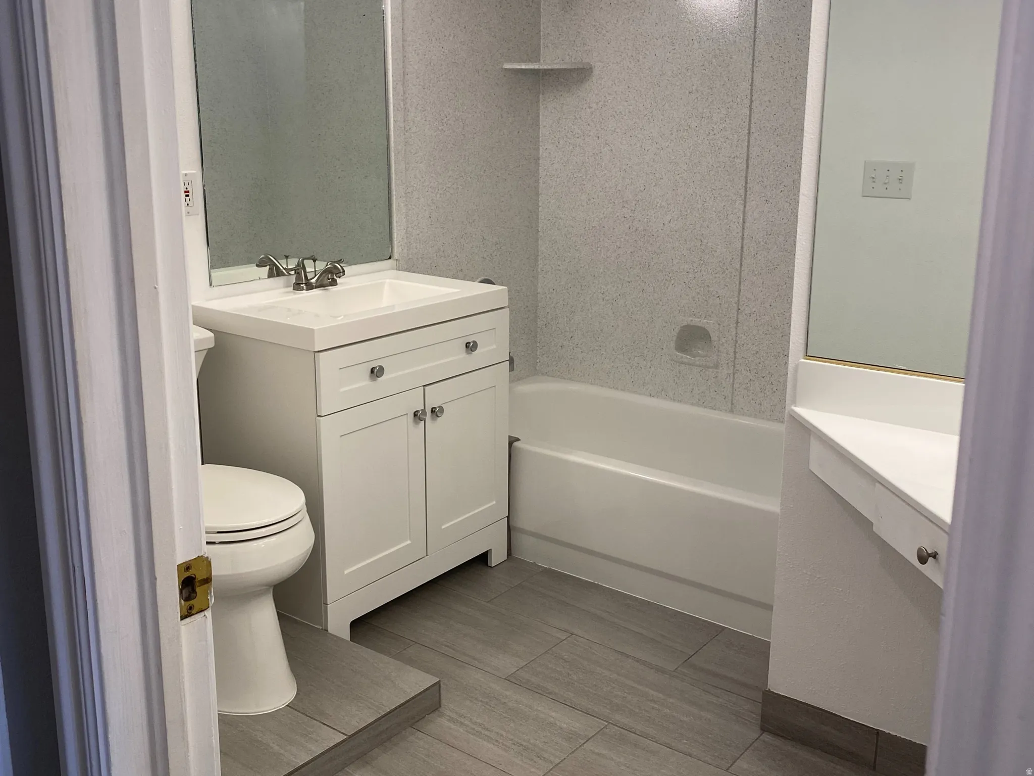 Ceramic tile flooring, white vanity with integrated sink, chrome faucet, white bathtub, and vanity lighting