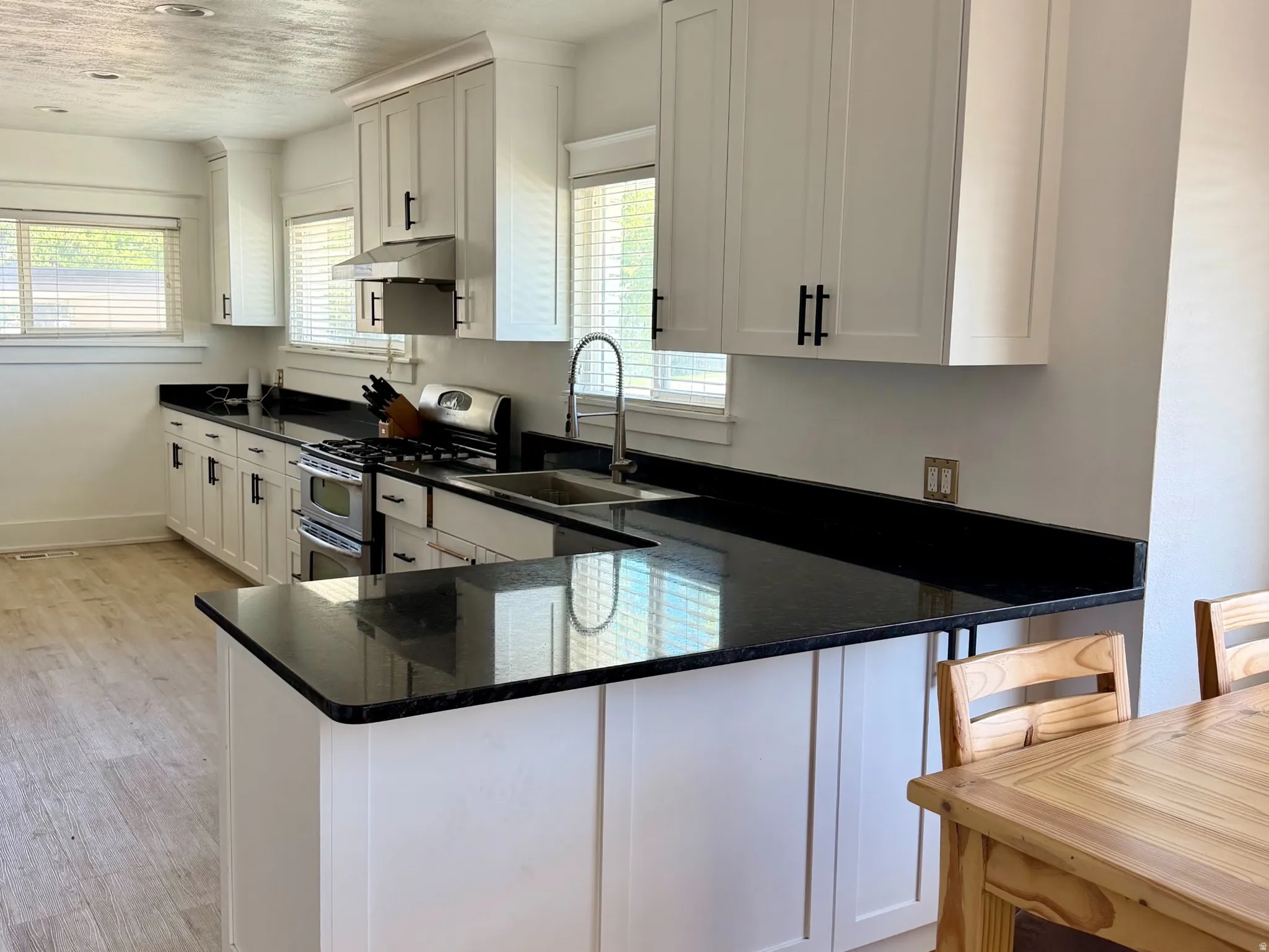 White shaker cabinetry, black countertops, stainless steel appliances, wood-finish flooring, and recessed lighting