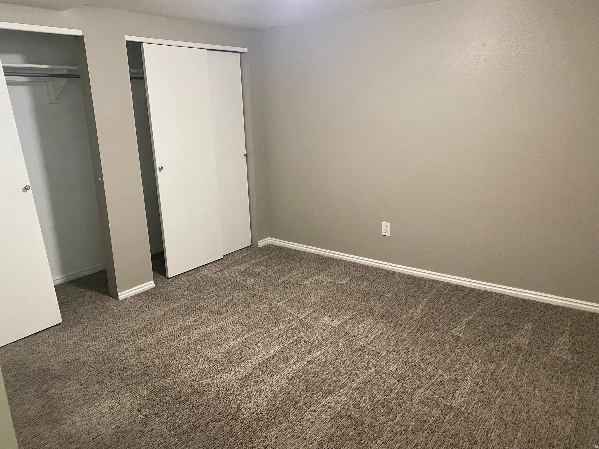 Wall-to-wall carpeting, neutral wall color, white baseboards, and two sliding closet doors