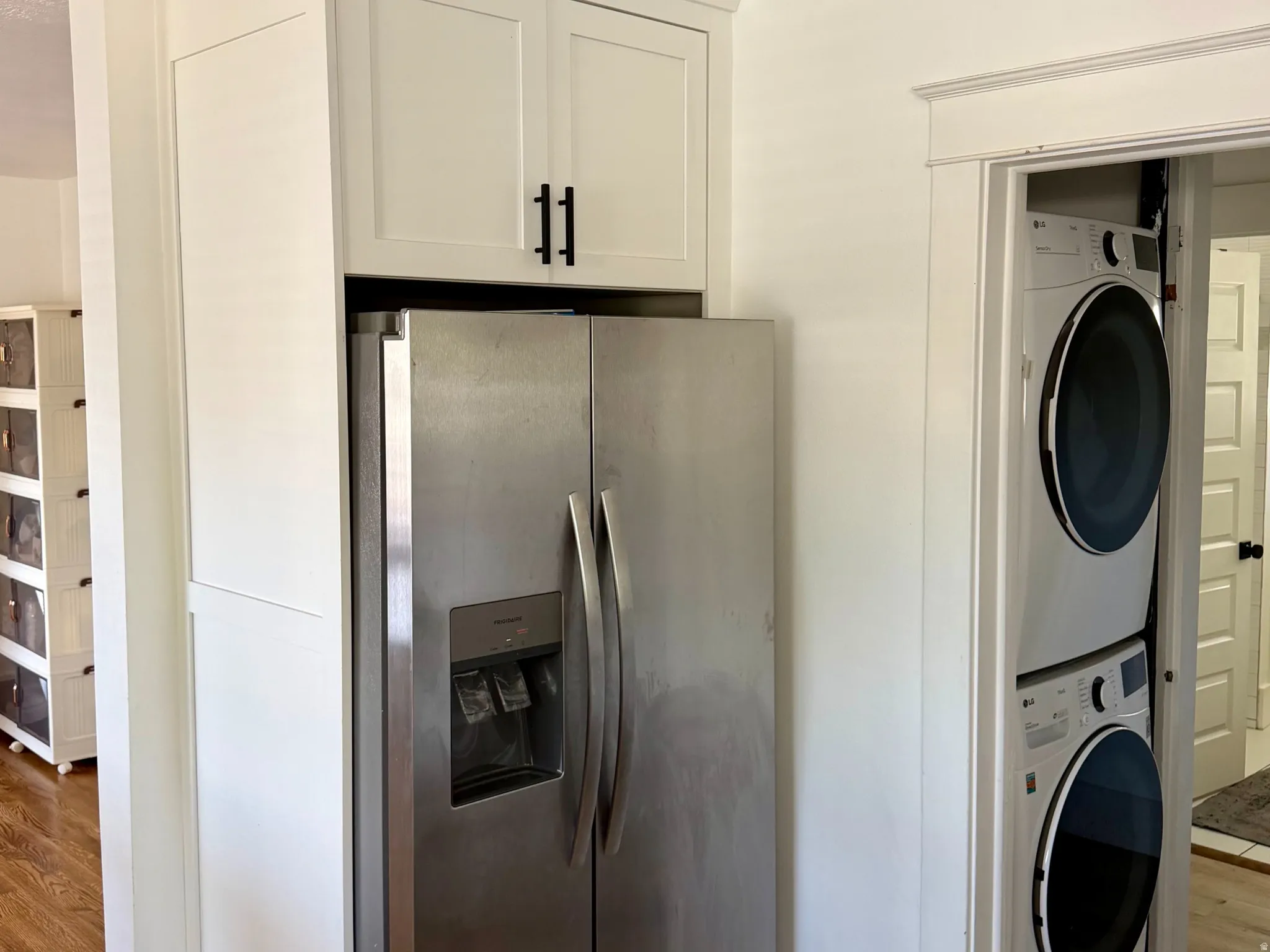 Stainless steel side-by-side refrigerator, white shaker-style cabinetry with matte black hardware, and wood-finish flooring