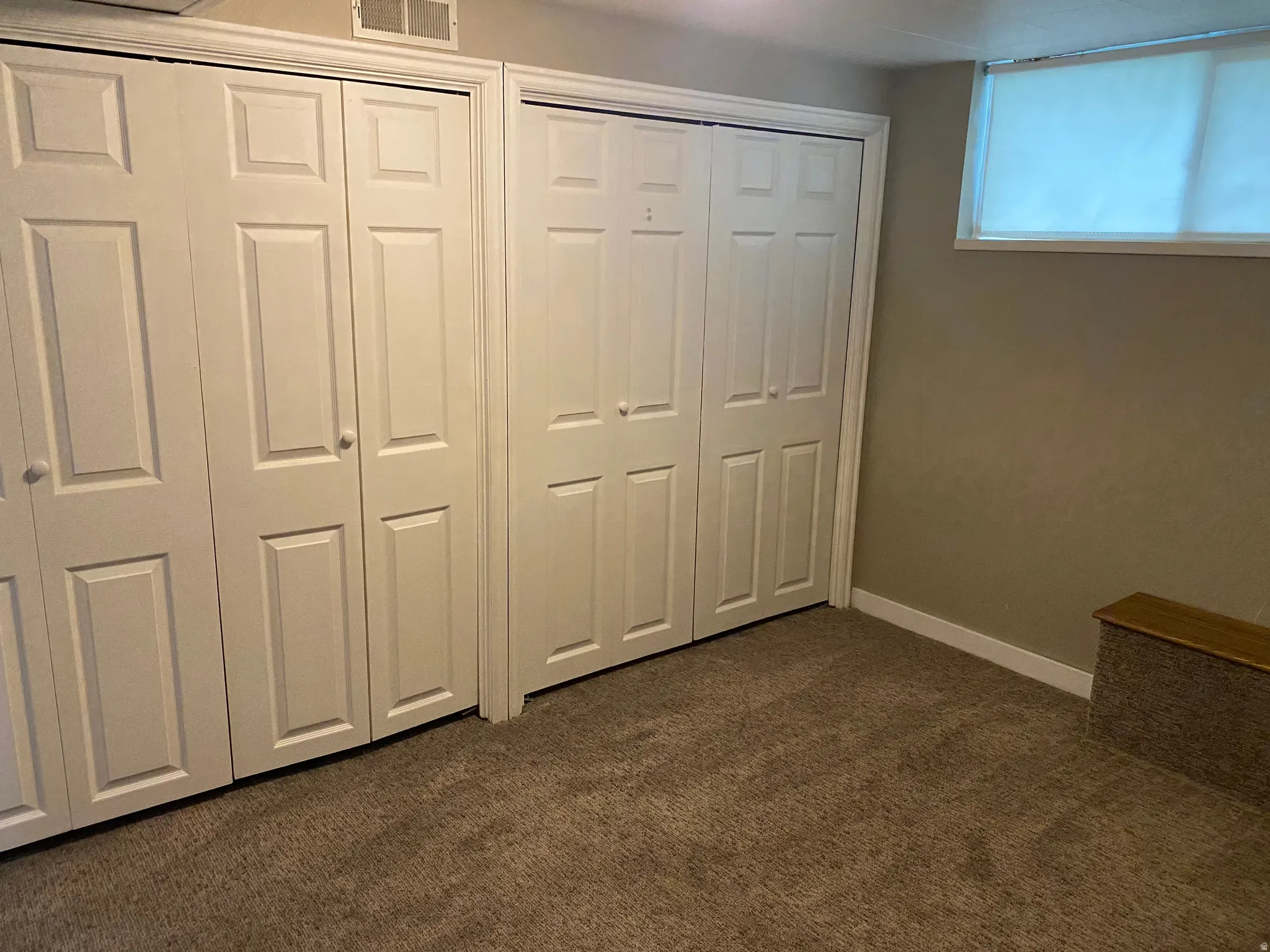 Multiple bi-fold panel doors, carpeted flooring, and a single window with a roller shade
