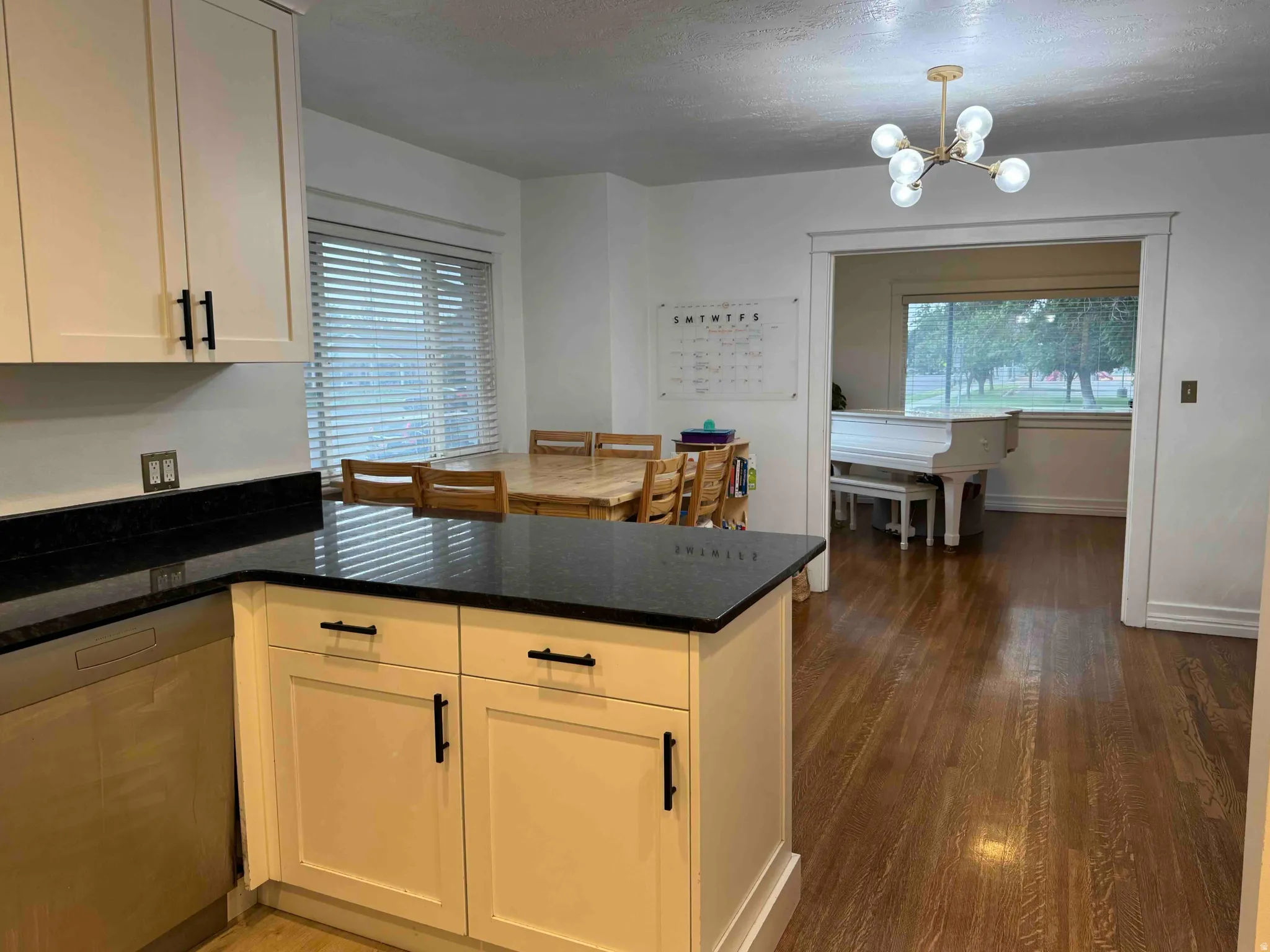White cabinetry with matte black hardware, dark countertops, built-in dishwasher, wood-finish flooring, and a modern ceiling light fixture