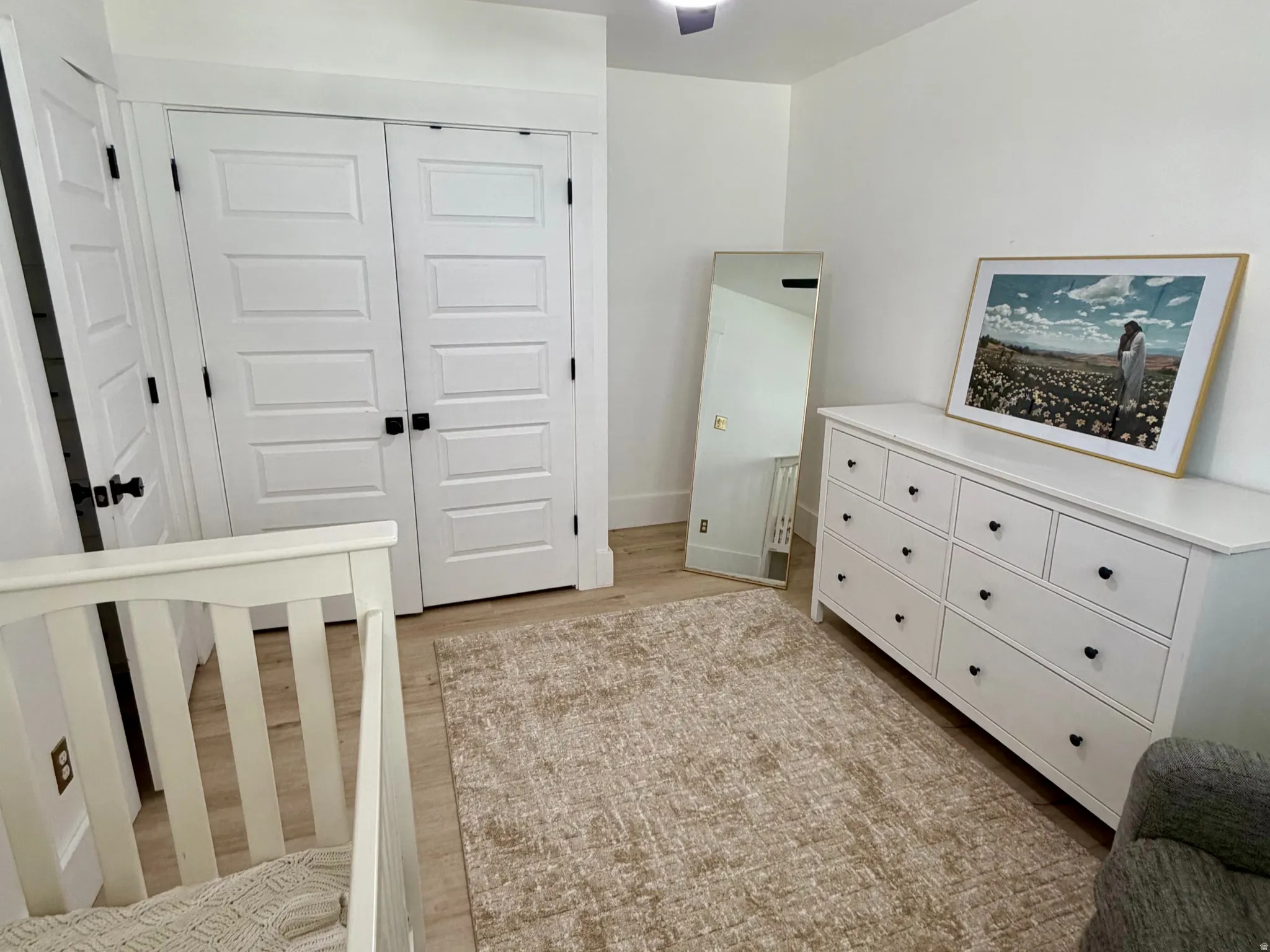Light-toned wood-finish flooring complements white walls, featuring a black ceiling fan with integrated lighting