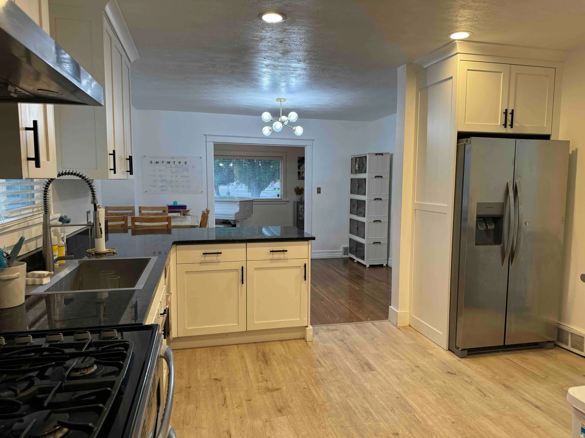 Light wood-finish flooring, white cabinetry with dark hardware, dark stone countertops, and stainless steel appliances