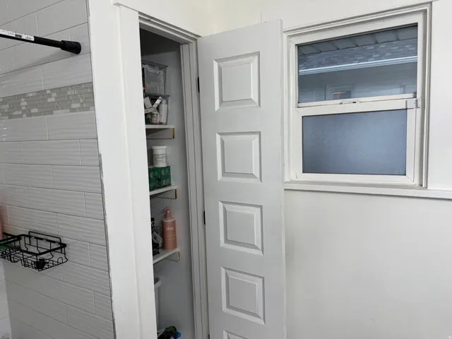 Bathroom featuring subway tile shower surround, white six-panel door with raised molding, and a window with blinds providing natural light