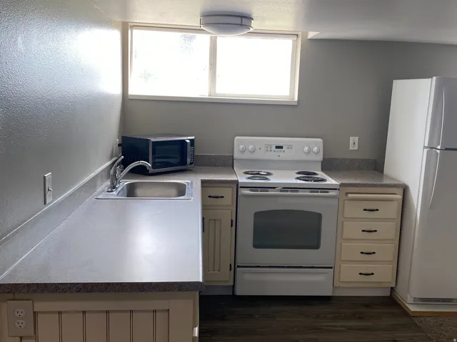 Kitchen featuring wood-finish flooring, white appliances, light countertops, and built-in cabinetry with dark hardware