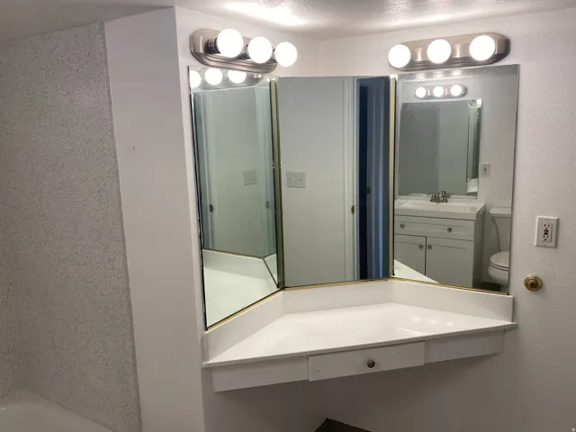 Vanity area featuring a three-panel mirror, built-in countertop, and integrated drawer