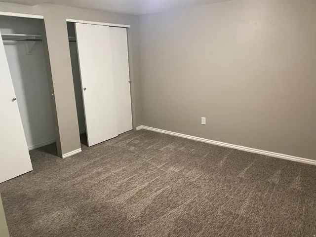 Wall-to-wall carpeting, neutral wall color, white baseboards, and two sliding closet doors