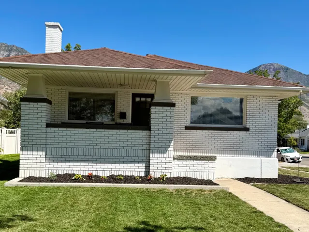 White brick exterior with a brown shingle roof, complemented by a concrete walkway