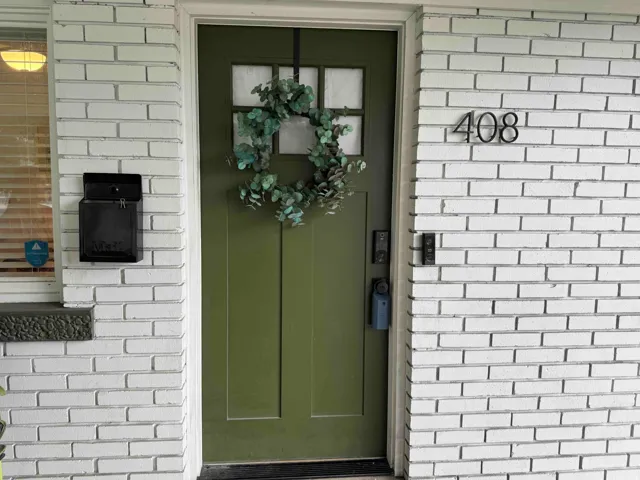 Painted brick exterior featuring a panelized entry door, black wall-mounted mailbox, and numerical house signage