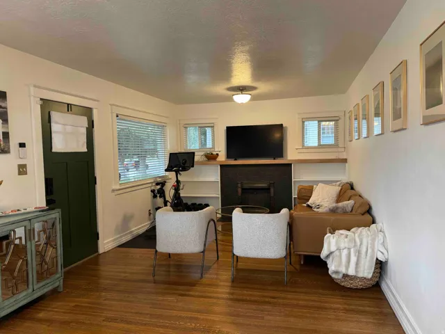 Bright, open living space featuring hardwood flooring, a gas fireplace with surround, built-in cabinetry with glass-front doors, and recessed ceiling lighting