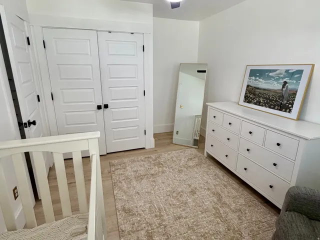 Light-toned wood-finish flooring complements white walls, featuring a black ceiling fan with integrated lighting
