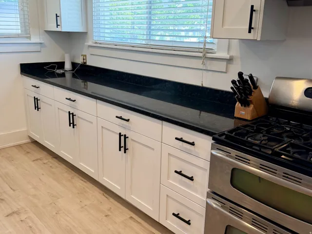 White shaker-style cabinetry with black hardware, dark countertops, a stainless steel range with a ventilation hood, and wood-finish flooring