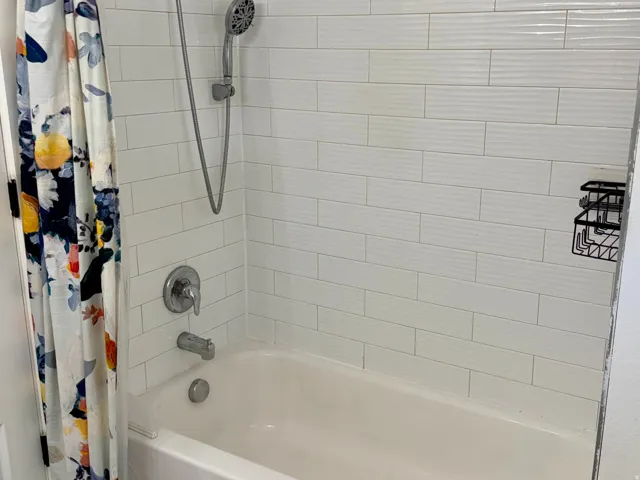 Bathtub with subway tile surround, mosaic tile accent, rainfall showerhead, and handheld shower sprayer