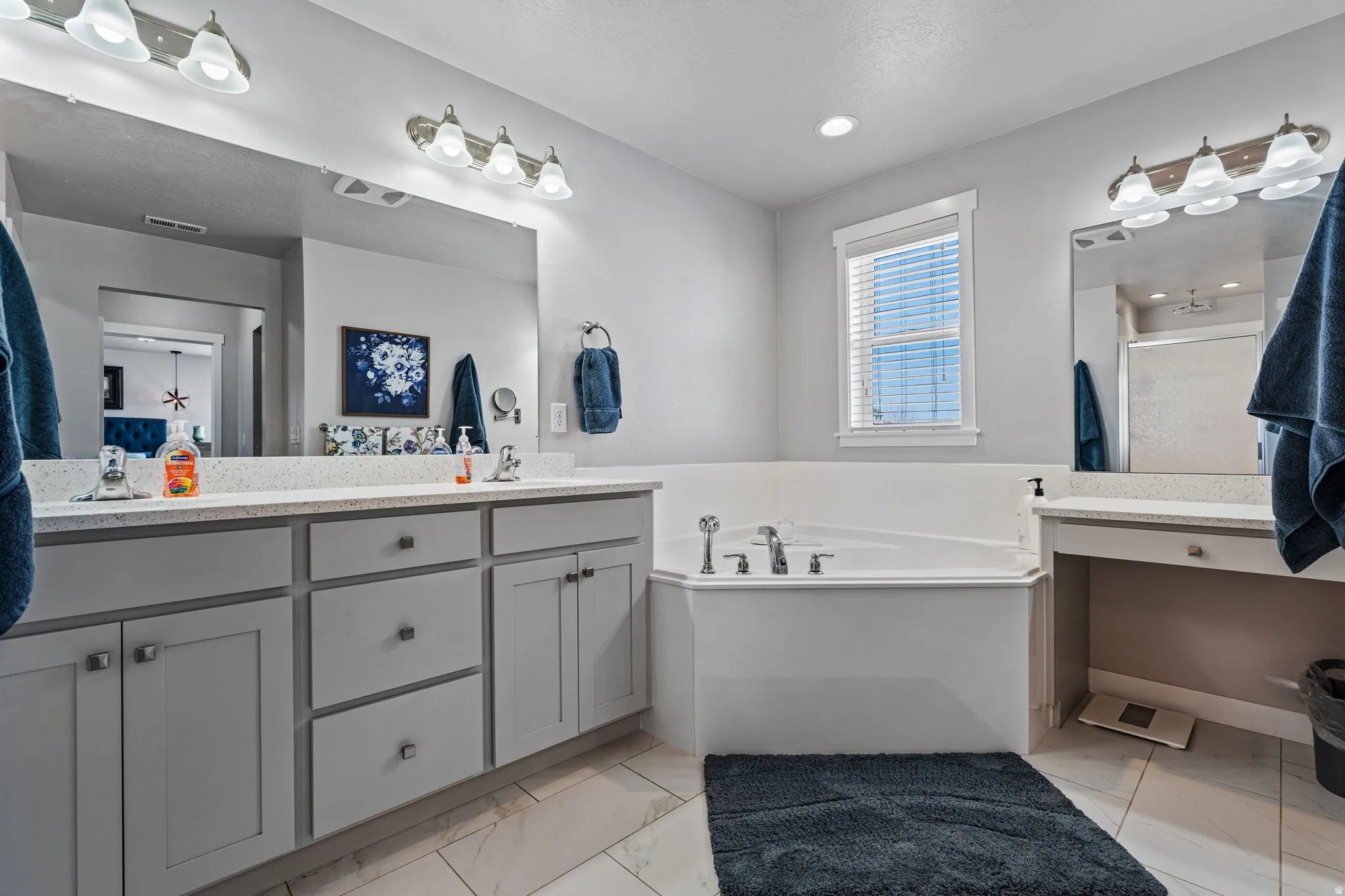 Dual vanity with light gray cabinetry, built-in soaking tub, tile flooring, and a large mirror