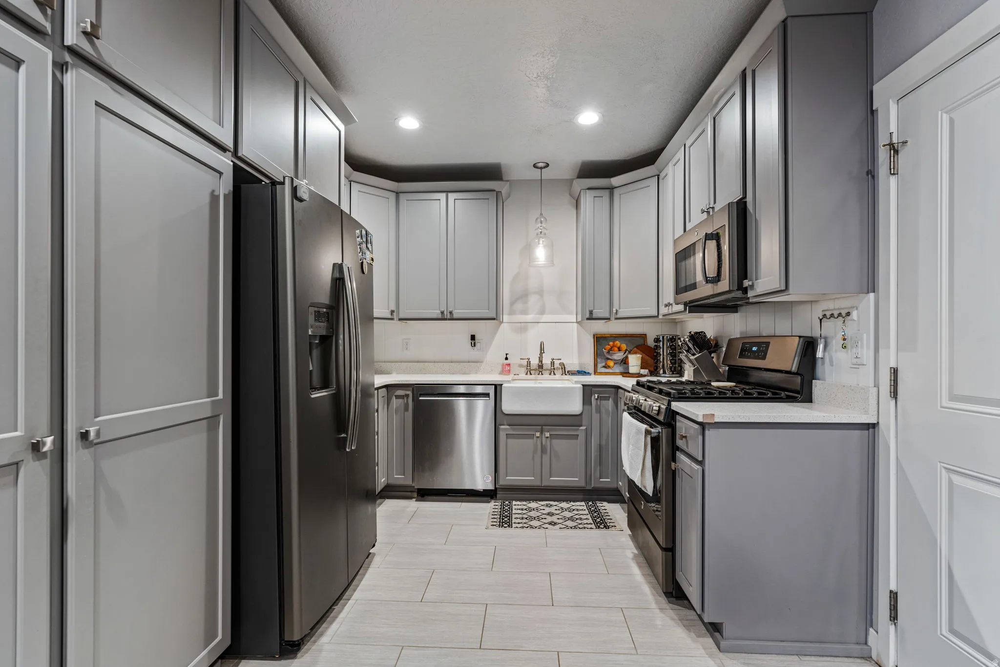 Kitchen featuring gray shaker-style cabinetry, stainless steel appliances, white subway tile backsplash, and light-toned countertops