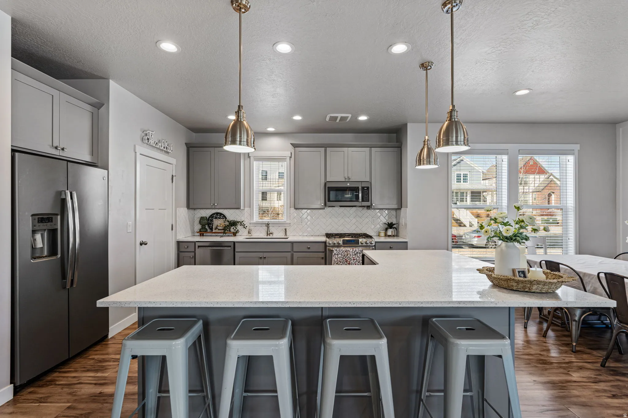 Kitchen featuring a large central island with seating, stainless steel appliances, grey cabinetry, a tile backsplash, and wood-finish flooring