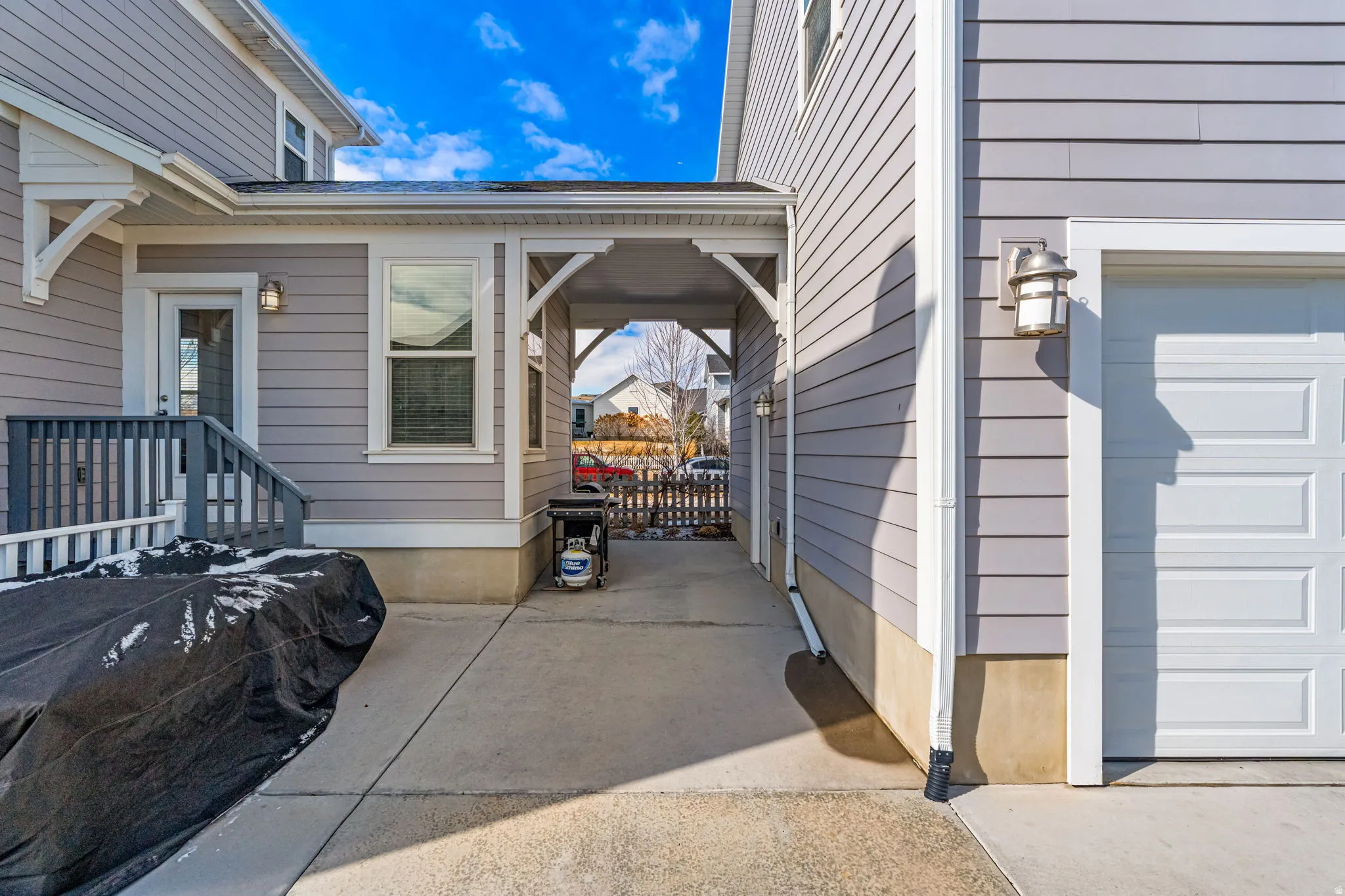 Attached garage with panel door, exterior lighting, concrete patio, covered walkway, and rear entry door with steps