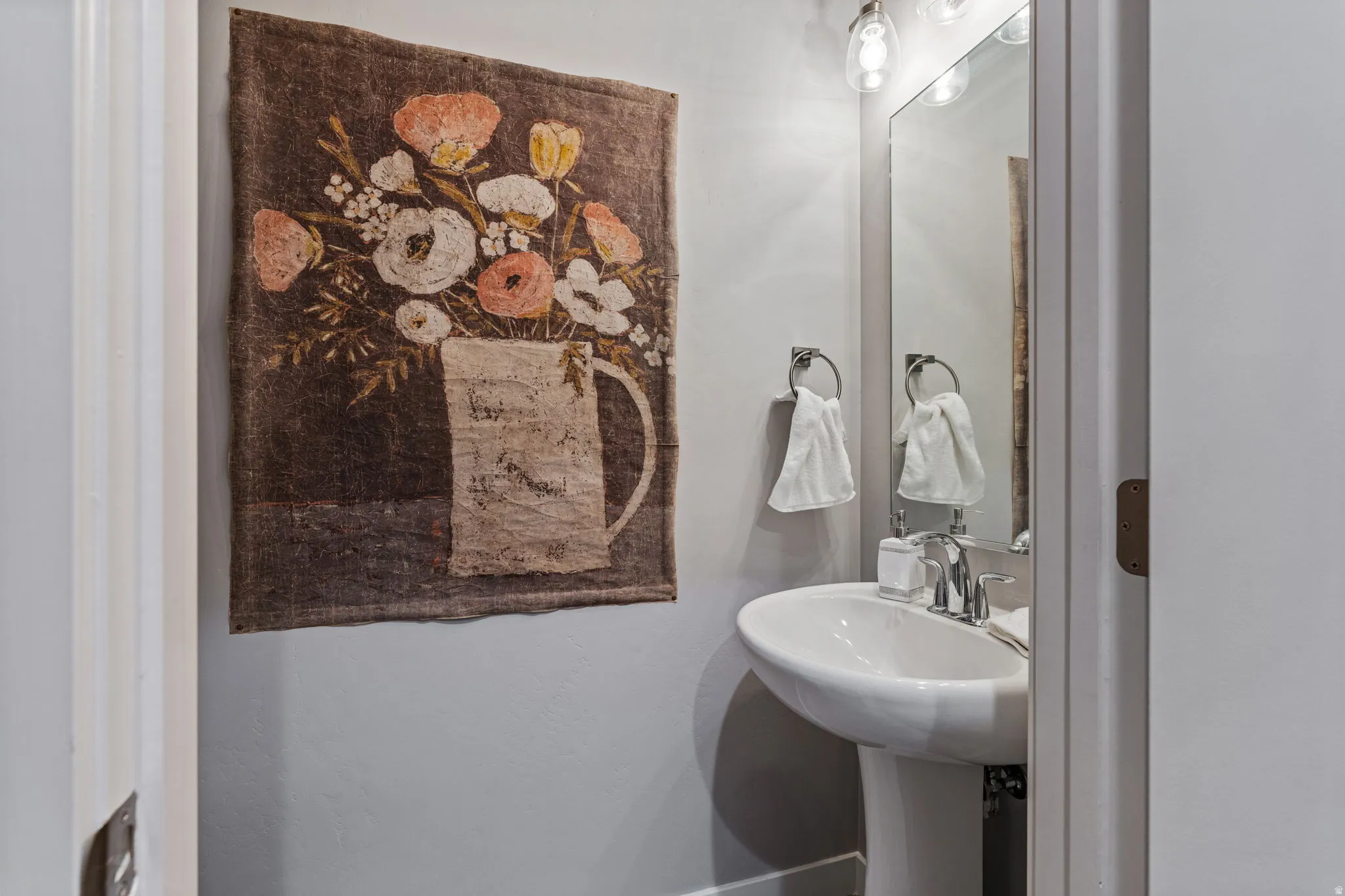 Pedestal sink with a chrome faucet, large rectangular mirror, and overhead vanity lighting