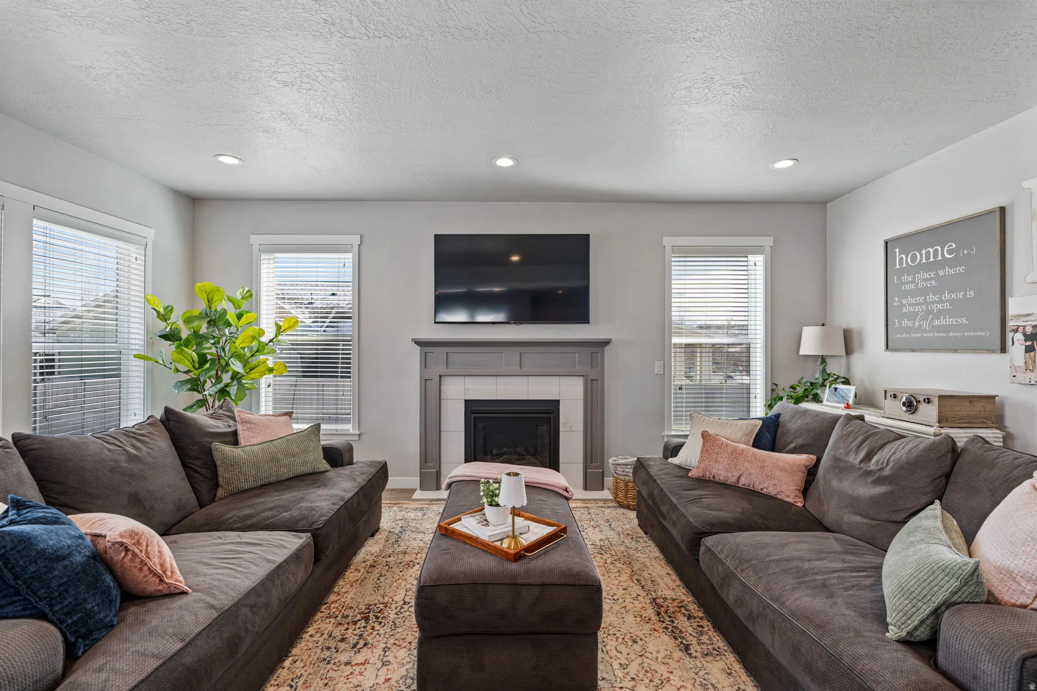 Recessed lighting, light gray wall color, multiple windows, fireplace with white tile surround, and a gray mantelpiece