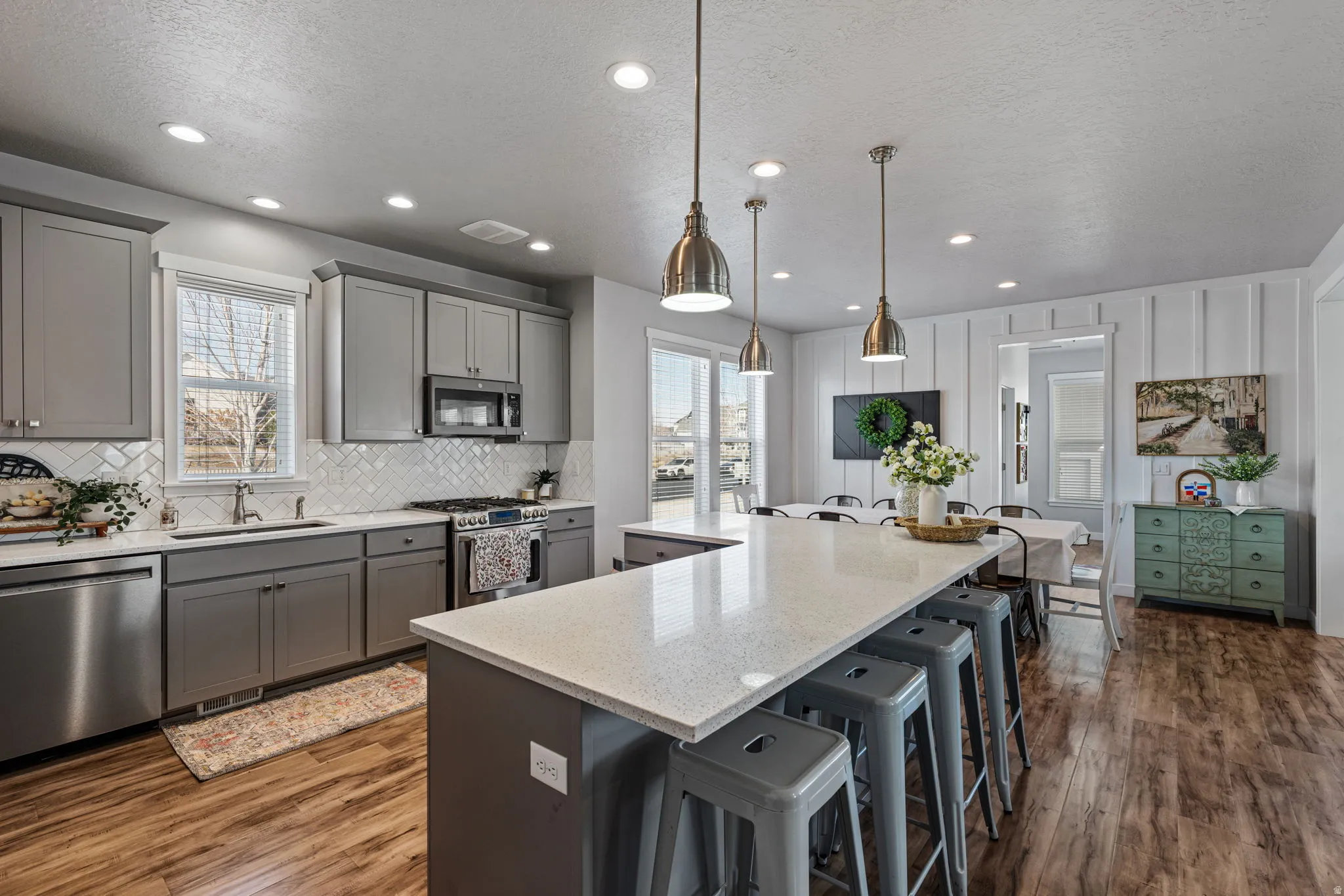 Spacious kitchen featuring gray shaker-style cabinetry, stainless steel appliances, a white tile backsplash, and wood-finish flooring