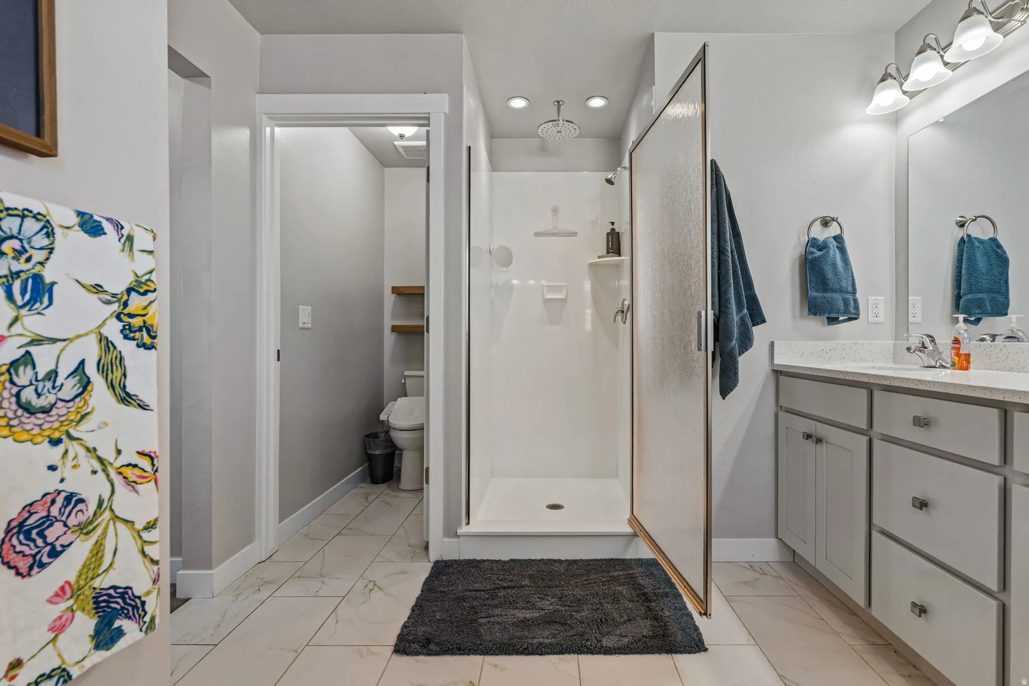 Spacious bathroom featuring a glass-enclosed shower, dual vanity with undermount sinks, and tile flooring
