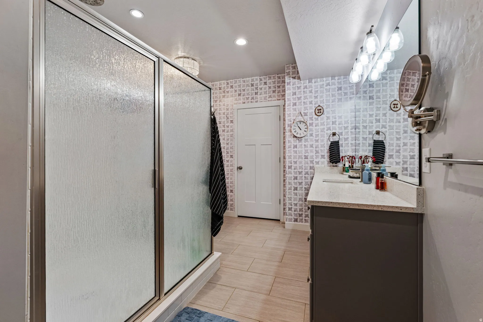 Walk-in shower with textured glass enclosure, single vanity with light-toned countertop, and patterned accent wall