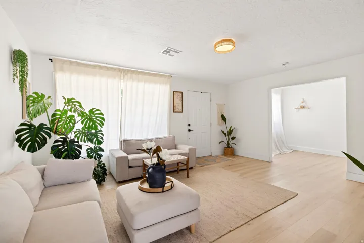 Spacious living area featuring light wood-finish flooring, white walls, and a round flush-mount ceiling light