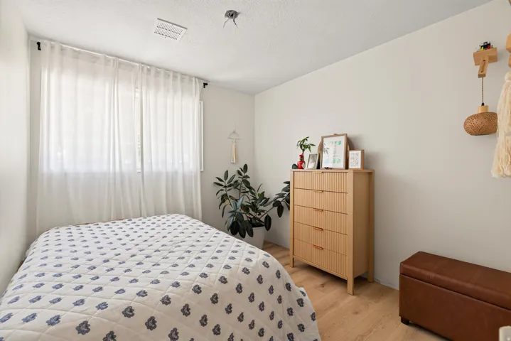 Wood-finish flooring with neutral wall tones and a window with sheer curtains