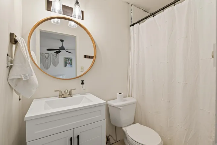 Contemporary bathroom featuring a white vanity with drawer storage and brushed nickel hardware, white ceramic vessel sink, and a wood-framed round mirror