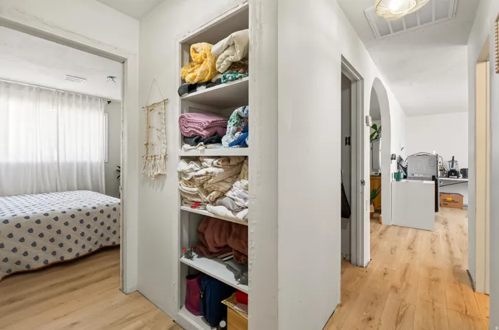 Hallway with wood-finish flooring, built-in shelving, and arched entryway