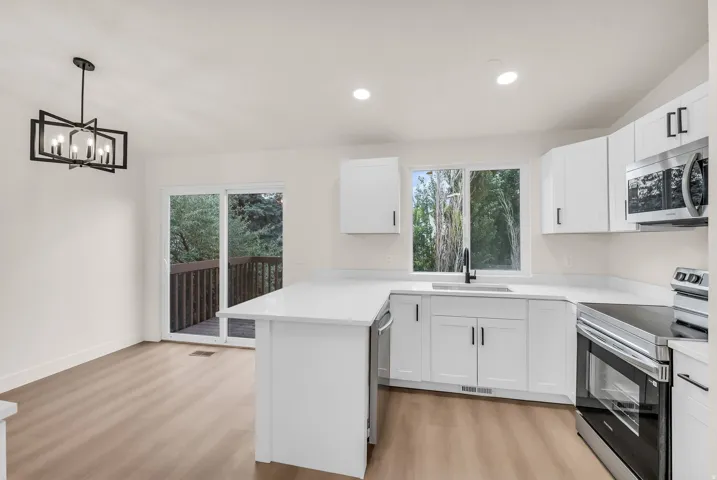 Modern kitchen featuring white cabinetry, light-toned countertops, stainless steel appliances, and wood-finish flooring