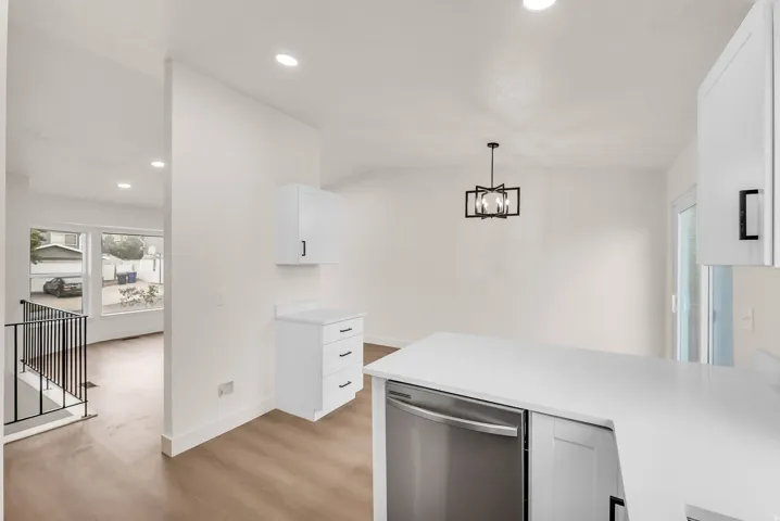 White cabinetry with black hardware, stainless steel dishwasher, white countertops, recessed lighting, and a contemporary chandelier
