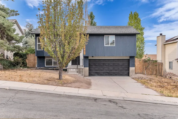 Split-level residence featuring a two-car garage, dark blue siding, and a fenced side yard