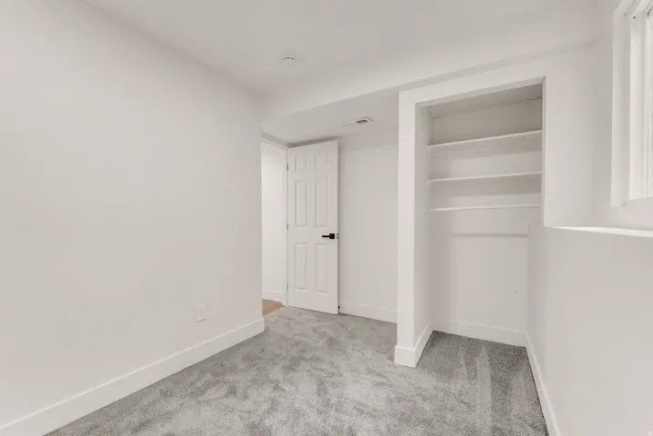 Carpeted interior space featuring an open closet with shelving and hanging rod, white trim, and a white interior door with black hardware