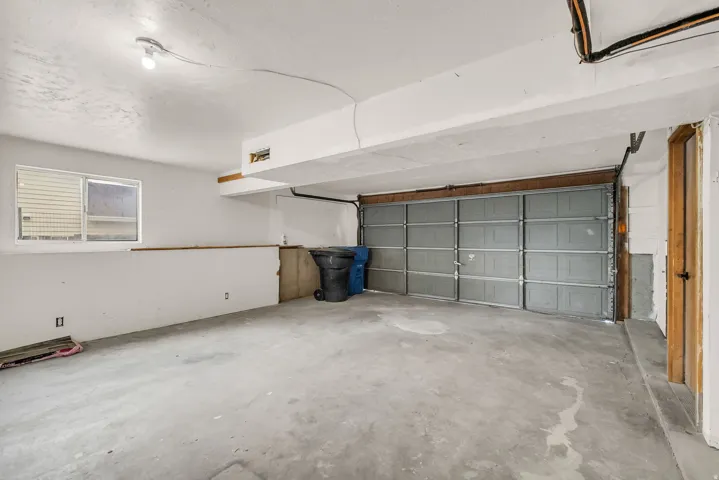 Concrete flooring, exposed ceiling beams, single light fixture, single window, garage door