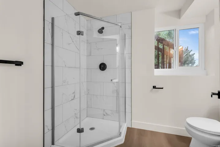 Glass-enclosed shower with white tiled walls, black fixtures, and a corner design