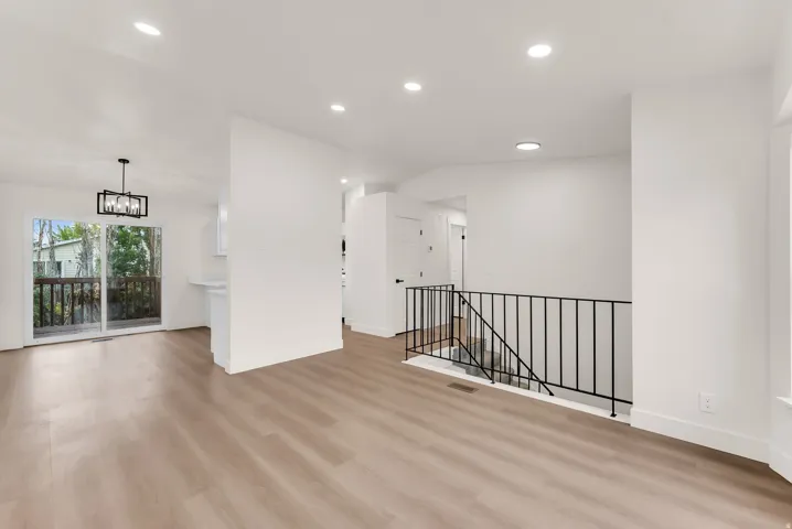 Expansive room with wood-finish flooring, recessed lighting, and a modern black metal staircase railing