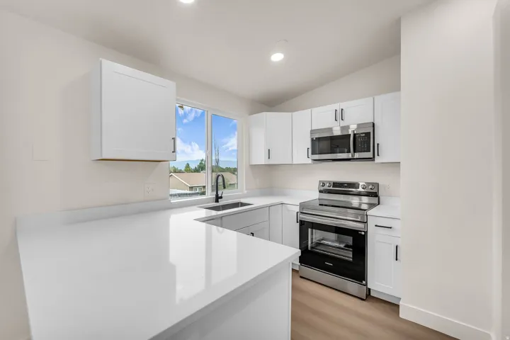White shaker cabinetry, stainless steel appliances, white countertops, wood-finish flooring, and recessed lighting